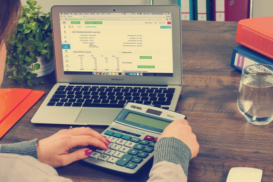 Pessoa fazendo contas na calculadora ao lado do notebook com planilha