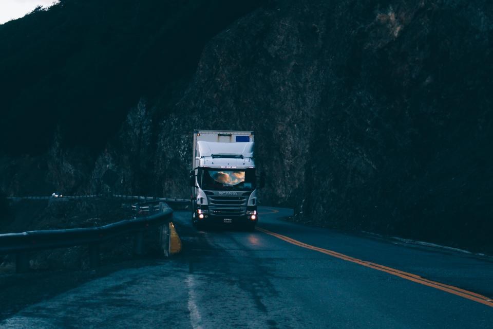 Caminhão de carga com os faróis acesos numa estrada de serra