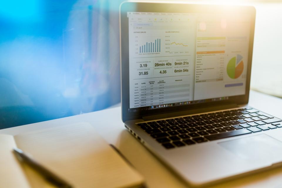 Notebook com gráficos financeiros na tela, sobre mesa clara