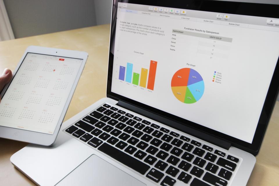 Notebook e tablet com gráficos de barras e pizza de um relatório