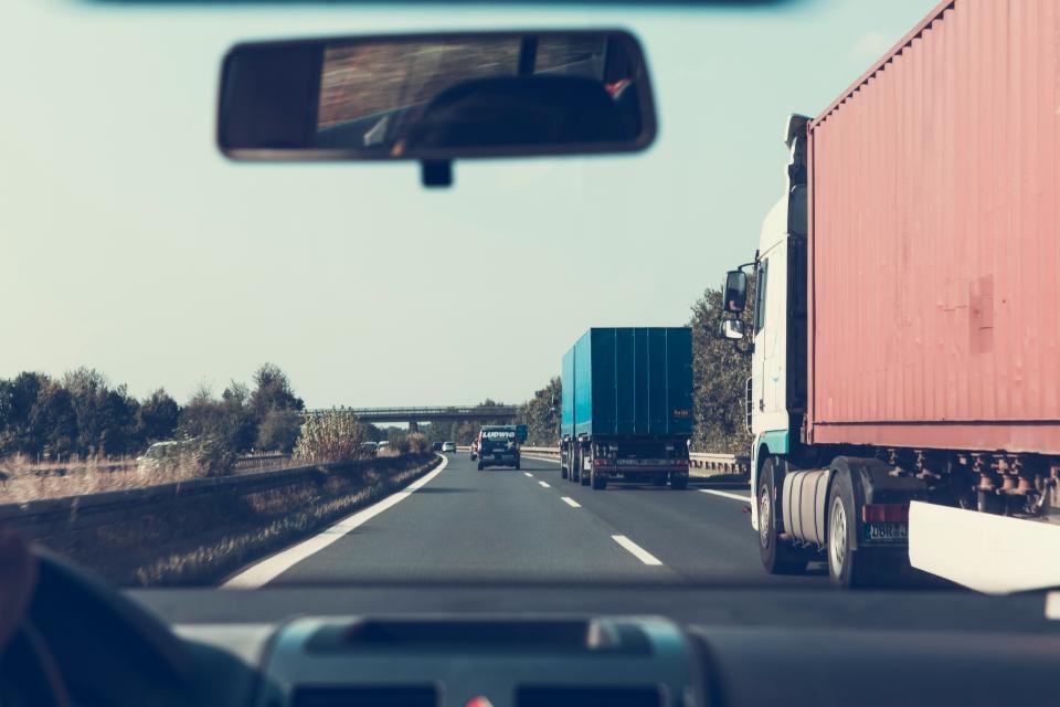 Caminhões de carga trafegando numa rodovia vistos de dentro de um veículo